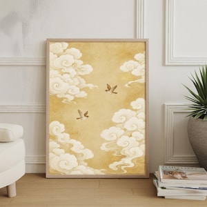 May include: Framed art print featuring a serene scene of birds in flight amidst fluffy white clouds against a warm, golden-yellow background. The artwork is encased in a light-colored wooden frame, adding a touch of elegance to the piece.