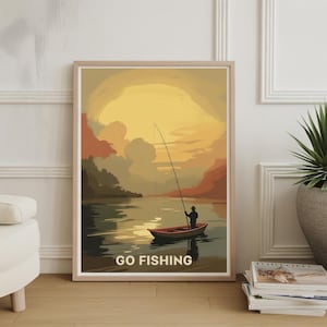 Puede incluir: Una impresión artística enmarcada representa a una persona pescando desde un bote en un lago al atardecer. La obra de arte presenta colores cálidos, incluyendo naranja, amarillo y marrón. Las palabras "GO FISHING" están impresas en la parte inferior de la imagen.