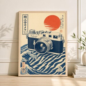 May include: A framed print featuring a vintage camera design. The artwork showcases a classic camera with a detailed lens, set against a backdrop of a rising sun and stylized ocean waves. Japanese text and the "Seikosha" logo are also visible.