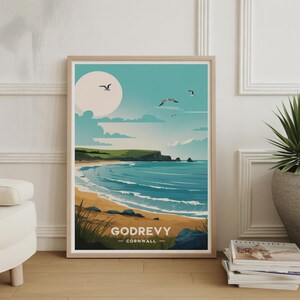 May include: A framed art print featuring a coastal landscape with a sandy beach, blue ocean, and green cliffs under a bright sky. The print includes the text "GODREVY - CORNWALL" and depicts seagulls in flight.