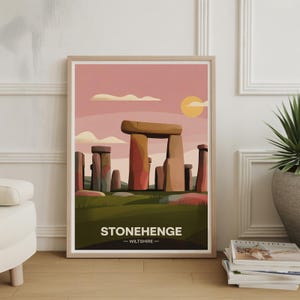 May include: Framed art print featuring a stylized illustration of Stonehenge. The artwork depicts the monument under a pink sky with a yellow sun and clouds. The text "STONEHENGE - WILTSHIRE" is at the bottom. The print is in a light wood frame.