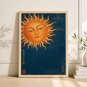 May include: A framed art print featuring a stylized sun with a serene face, rendered in shades of orange and yellow against a deep blue background. The artwork has Japanese text and a red seal. The frame is a light wood color.