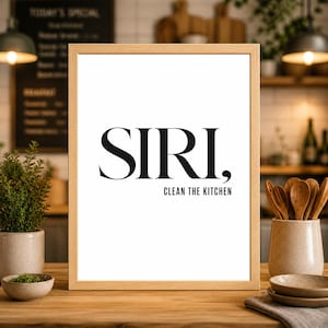 Może przedstawiać: Oprawiony wydruk z czarnym napisem "SIRI, CLEAN THE KITCHEN" na białym tle. Rama jest w jasnym kolorze drewna. Wydruk jest prezentowany na drewnianej powierzchni z elementami kuchennymi w tle.