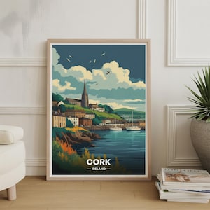May include: A framed art print showing a stylized illustration of Cork, Ireland. The image features a coastal town with a church spire, boats, and a harbour under a cloudy sky. The word "CORK" is printed at the bottom.