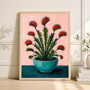 May include: A framed art print depicting a stylized painting of a Venus flytrap plant. The plant has red traps and green stems, set against a pink background. The plant is in a teal blue pot, and the frame is a light wood colour.