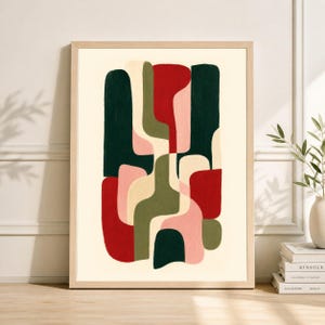 May include: Abstract art print in a light wood frame. The artwork features a composition of organic shapes in dark green, red, pink, and olive green against a cream background. The print is displayed on a wooden surface.
