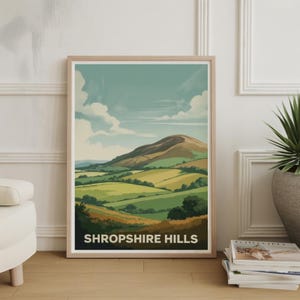 May include: A framed print featuring a landscape illustration of the Shropshire Hills. The artwork depicts rolling green hills, fields, and a mountain under a blue sky with fluffy white clouds. The text "SHROPSHIRE HILLS" is at the bottom.
