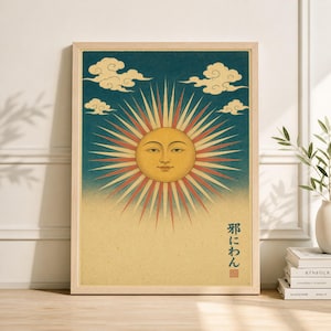 May include: Framed art print featuring a stylized sun with a serene face, radiating red and cream-colored beams against a blue sky. The artwork includes fluffy white clouds and Japanese text. The print is in a light wood frame.