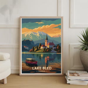 Könnte beinhalten: Ein gerahmter Kunstdruck vom Bleder See, Slowenien. Das Kunstwerk zeigt eine Seeszene mit einer Kirche auf einer Insel, Bergen und einem Boot. Der Himmel wechselt von Orange zu Blau. Der Text "LAKE BLED - SLOVENIA" steht unten.