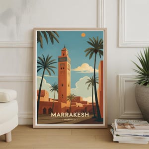 May include: Framed art print featuring a stylized illustration of Marrakech, Morocco. The artwork depicts a tall, orange minaret surrounded by palm trees under a blue sky with a yellow sun. The word "MARRAKESH" is printed at the bottom.