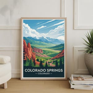 May include: A framed art print showcasing a landscape of Colorado Springs, Colorado. The artwork displays a valley with red rock formations, green hills, and snow-covered mountains under a blue sky with clouds. The text "COLORADO SPRINGS - COLORADO -" is at the bottom.