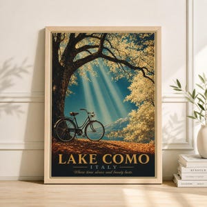 May include: A framed art print featuring a vintage bicycle under a large tree with sunlight streaming through the branches. The print has the words "Lake Como Italy" and the phrase "Where time slows and beauty lasts."
