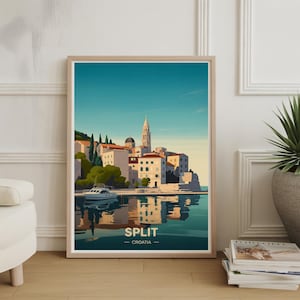 Op de afbeelding: Een ingelijste kunstprint met een kustlandschap van Split, Kroatië. Het kunstwerk toont witte gebouwen met rode daken, een kerktoren en een boot op het water. De tekst "SPLIT - CROATIA" staat onderaan de print.