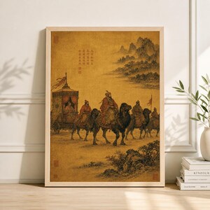 May include: A framed print of an ancient Chinese painting depicting a caravan of people riding camels through a desert landscape. The painting features figures in traditional attire, a carriage, and mountains in the background.