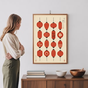 Puede incluir: Un cuadro enmarcado con faroles japoneses rojos sobre un fondo crema. Los faroles varían en forma y diseño, con algunos mostrando patrones florales y geométricos. Texto japonés visible en el cuadro.
