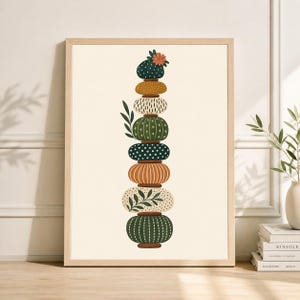 May include: A framed art print featuring a stacked arrangement of stylized, rounded shapes in various colors and patterns. The artwork includes shades of green, orange, and cream, with botanical accents and a small flower at the top. The print is in a light wood frame.