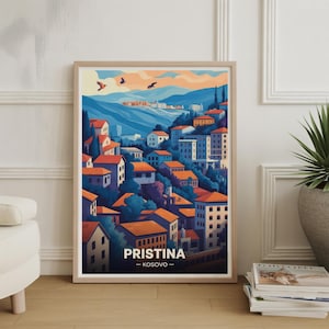 Può includere: Stampa artistica incorniciata di Pristina, Kosovo, con un'illustrazione stilizzata di un paesaggio urbano. L'opera mostra edifici con tetti arancioni, sullo sfondo di montagne blu e un cielo al tramonto. La stampa include il nome della città e del paese.