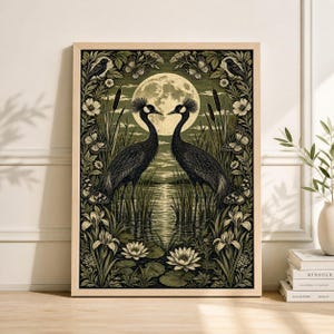 May include: Framed art print depicting two black crowned cranes, facing each other, with a full moon and a waterscape backdrop. The artwork is framed with floral and butterfly designs in green and cream tones.