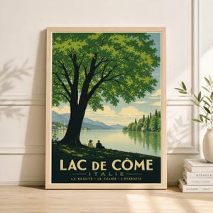 May include: A framed vintage travel poster for Lake Como, Italy. The poster features a large tree in the foreground, with a lake and mountains in the background. The text "LAC DE COME" is at the bottom, with additional text below.