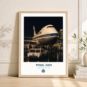 May include: A framed print featuring a vintage Pan Am Boeing 747-121 at an airport. The aircraft is white and blue, with the Pan Am logo visible. A small vehicle is in front of the plane. The print includes the text "PAN AM" and "NEW YORK, NY".