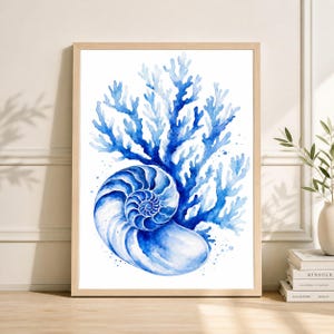 May include: Watercolor print of a nautilus shell and coral in shades of blue. The artwork is framed in a light wood frame. The nautilus shell is detailed with spiral patterns, and the coral is a branching design.
