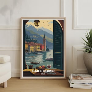 Peut inclure: Impression d'art encadrée du lac de Côme, en Italie, présentant une vue panoramique à travers une fenêtre. L'œuvre représente un lac avec des bateaux, des bâtiments colorés et des montagnes en arrière-plan. Une table avec des fruits et un verre de vin est au premier plan.