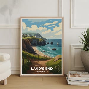 May include: A framed art print of Land's End, Cornwall. The landscape art features a coastal scene with a sandy beach, cliffs, and the ocean. The sky is blue with white clouds. The print is in a light wood frame.