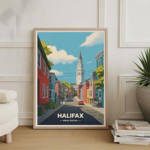 Puede incluir: Una impresión artística enmarcada de Halifax, Nueva Escocia, que presenta una escena callejera con edificios coloridos y una alta torre del reloj bajo un cielo azul con nubes. La palabra "HALIFAX" está impresa en la parte inferior.