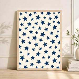 May include: A framed print featuring a repeating pattern of navy blue stars on a cream background. The stars vary in size and are evenly distributed across the surface. The frame is made of light-colored wood.