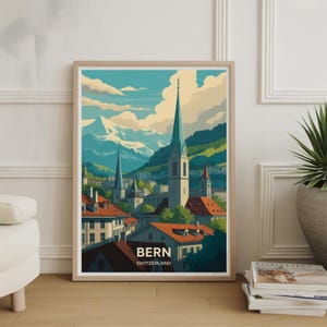 May include: A framed art print of Bern, Switzerland, featuring a stylized illustration of the city's architecture. The artwork showcases a cityscape with church spires, red-tiled roofs, and snow-capped mountains under a blue sky. The print is in a light wood frame.