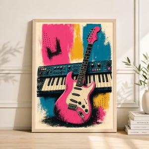 May include: A framed art print featuring a pink electric guitar leaning against a blue synthesizer keyboard. The background has bold strokes of pink, yellow, and blue. The artwork has a retro, pop art style.