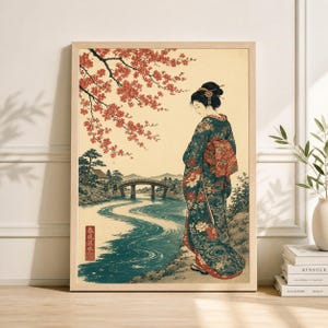 以下が含まれることがあります： 日本の芸術作品の額入りプリント。着物を着た女性が川のそばに立っており、背景には橋と桜があります。着物はティール色で花柄で、アートワークはヴィンテージ感があります。