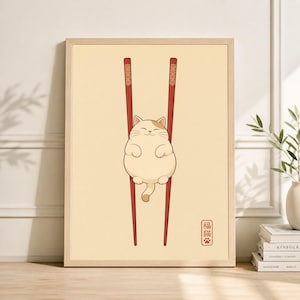 Puede incluir: Una impresión enmarcada que presenta un gato de dibujos animados sostenido entre dos palillos rojos. El gato es blanco con marcas marrones y una cara sonriente. El fondo es de color amarillo claro, con texto japonés en un cuadrado rojo.