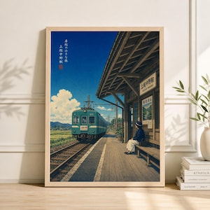 Op de afbeelding: Een ingelijste prent van een Japanse treinstationscène. Een turquoise trein staat op de rails en een persoon zit op een bank onder een houten schuilplaats. De lucht is blauw met witte wolken. De prent heeft Japanse tekst.
