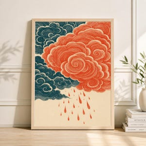 May include: A framed art print featuring a stylized illustration of clouds and rain. The artwork showcases a contrast between dark teal and orange clouds, with orange raindrops falling below. The print is set against a cream-colored background.