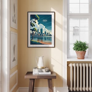 May include: Framed art print featuring a stylized depiction of Perth, Australia, with a cityscape reflected in the water. The artwork includes the text "PERTH AUSTRALIA" and is set against a blue sky with clouds. The print is displayed on a wall.