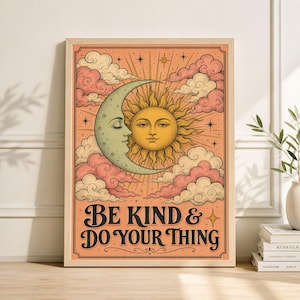 May include: A framed art print featuring a vintage-style illustration of a smiling sun and a crescent moon with a face, set against a backdrop of pink clouds and stars. The text "BE KIND & DO YOUR THING" is displayed in a decorative font.