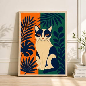 May include: A framed art print featuring a stylized cat illustration. The cat is white with black markings and orange eyes, set against a split background of orange and green. Dark blue foliage surrounds the cat, creating a vibrant, decorative piece.