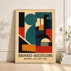 May include: Framed Bauhaus-Ausstellung poster. The artwork features geometric shapes in teal, black, orange, red, and blue. The poster includes the text "BAUHAUS-AUSSTELLUNG WEIMAR, JULI-SEPT. 1923" in a serif font. The frame is a light wood color.