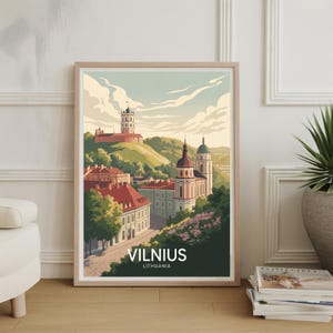 May include: A framed art print featuring a stylized illustration of Vilnius, Lithuania. The artwork depicts a cityscape with buildings, churches, and a tower on a hill, under a cloudy sky. The print includes the text "VILNIUS LITHUANIA".