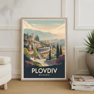 May include: A framed art print featuring a stylized illustration of Plovdiv, Bulgaria. The artwork depicts a scenic view of the city with buildings, a colonnade, and mountains in the background. The print has a dark blue banner with the city name and country.