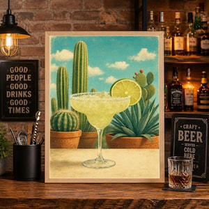 May include: A framed print depicting a margarita cocktail with a lime slice, set against a backdrop of cacti and a blue sky with clouds. The artwork has a vintage style, evoking a desert theme.