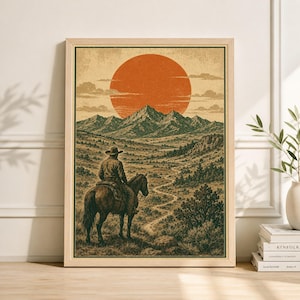 Puede incluir: Una impresión enmarcada de estilo vintage representa a un vaquero a caballo, sobre un fondo de montañas y un gran sol naranja. La obra presenta un paisaje detallado con un camino sinuoso, evocando el Oeste americano.