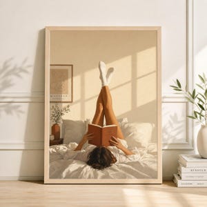 May include: A framed print shows a person reading in bed with their legs raised, wearing white socks. The room has a neutral colour palette, with a framed artwork and a vase of greenery. The book is brown.