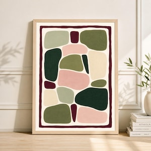 May include: Abstract art print in a light wood frame. The artwork features organic shapes in shades of green, pink, and cream, outlined with a dark red border. The shapes are arranged against a cream background.