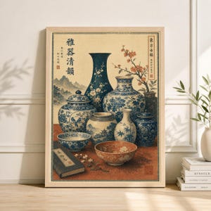 Op de afbeelding: Een ingelijste prent met een stilleven van blauw-witte porseleinen vazen, kommen en een boek. De vazen tonen bloemmotieven en zijn gerangschikt op een rode ondergrond. Het kunstwerk heeft een traditionele Aziatische esthetiek.