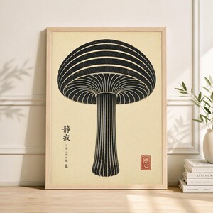 May include: A framed art print featuring a stylized black mushroom illustration on a cream background. The artwork includes Japanese text and a red seal. The mushroom has a striped cap and stem, with a minimalist aesthetic.