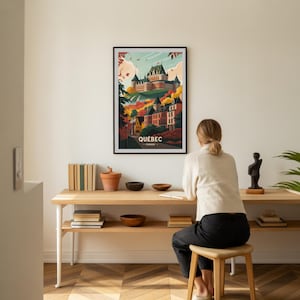 May include: A framed art print showcasing a stylized illustration of Quebec City, Canada. The artwork depicts a castle atop a hill, surrounded by autumn foliage and buildings. The word "QUEBEC" is printed at the bottom of the print.