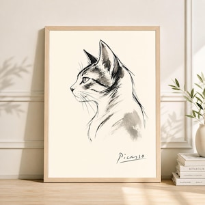 Puede incluir: Dibujo a tinta en blanco y negro enmarcado de un perfil de gato, firmado "Picasso". La obra presenta un estilo minimalista con líneas finas y sombreado, sobre un fondo crema. El marco es de color madera clara.