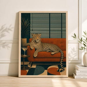 May include: A framed art print featuring a leopard lounging on a rust-colored sofa. The leopard is the focal point, with a cocktail on a side table. The background includes a dark wall, blinds, and a potted plant, creating a stylish, vintage vibe.